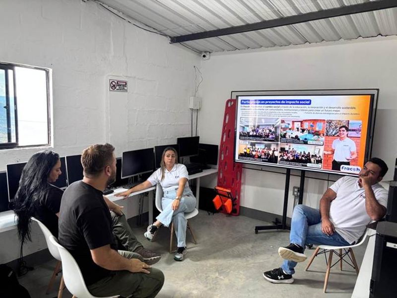 El aula de tecnología actual de la fundación: computadores de escritorio en mesas contra la pared y un televisor, durante una visita del equipo de Fracoh Group.