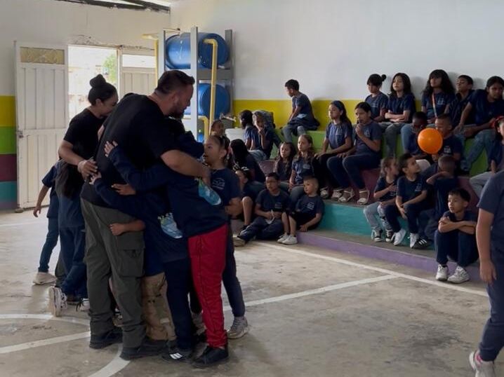 Un formador abraza a varios niños en la cancha de la fundación, mientras otros miran desde las gradas.