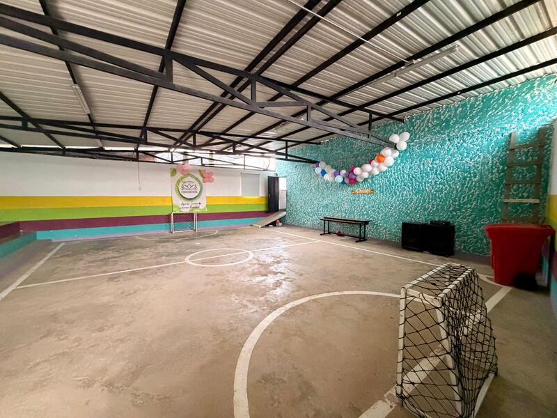 La cancha cubierta de la fundación, vacía: piso de cemento, un arco pequeño y un mural verde al fondo.