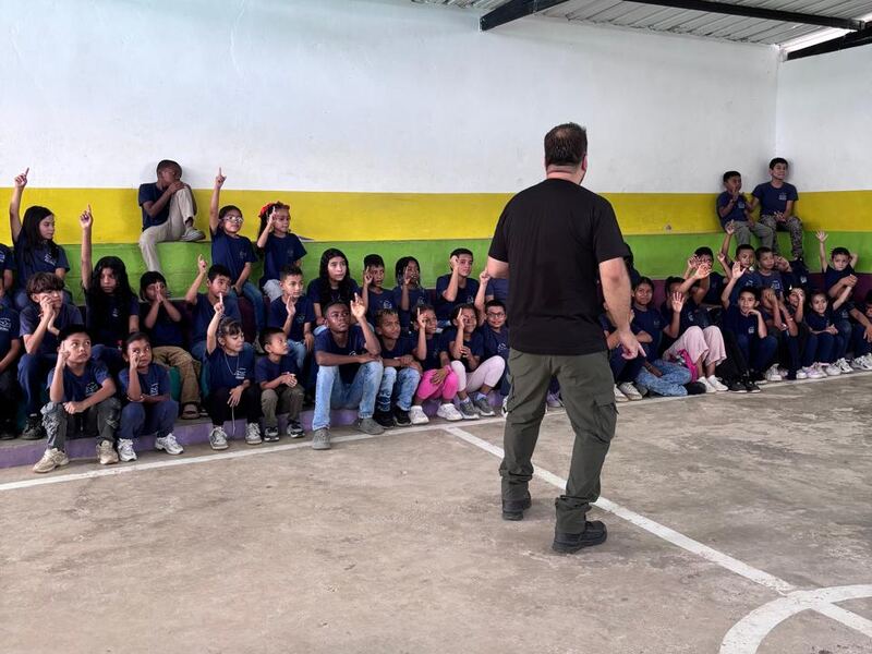 Niños levantan la mano en las gradas de la cancha mientras un formador les habla.