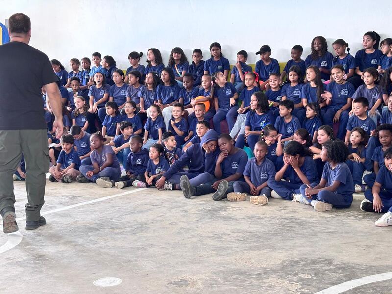 Decenas de niños y jóvenes con la camiseta de la fundación, sentados en la cancha escuchando a un adulto.