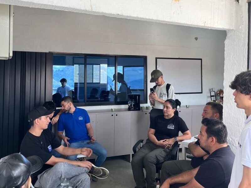 Un grupo de personas conversa sentado en un salón de la fundación; un hombre de pie habla frente a un tablero blanco.