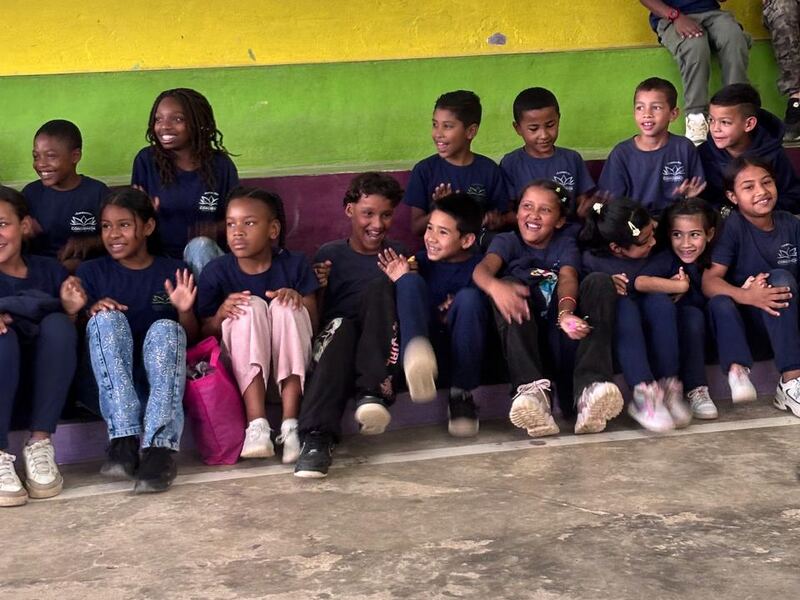 Un grupo de niños y niñas sonríe sentado en las gradas de colores de la fundación.